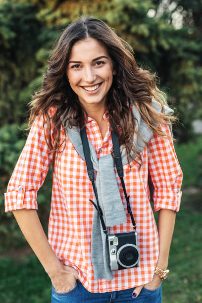 Beautiful girl photographer with camera looking at camera and smiling. She is wearing casual clothing, taking photos with her beautiful analog film camera. Close-up image of urban female photographer