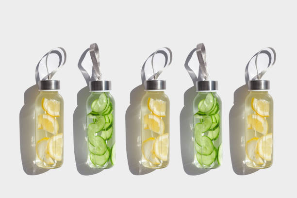 istock Glass bottles with lemon, cucumber water drink detox at sunlight on white, creative pattern. Healthy infused water boost metabolism, weight loss. Aesthetic still life, refreshing drink 2199371842