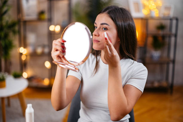 istock Young Woman Using A Gua Sha Stone While Looking In A Hand Mirror In The Living Room 2199374434