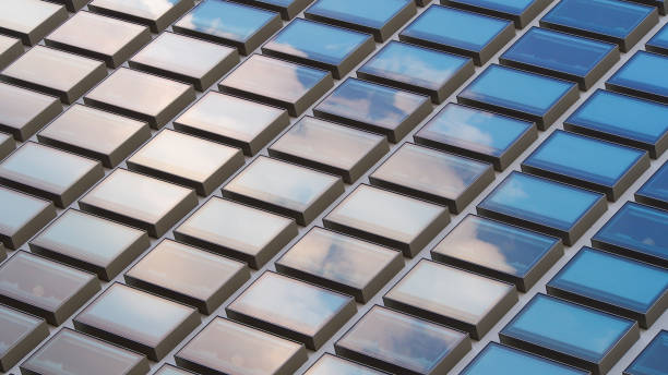 a grid of reflective glass panels arranged in a diagonal pattern. The panels alternate between soft beige and vivid blue tones, mirroring the surrounding sky and creating a dynamic interplay of light and reflection