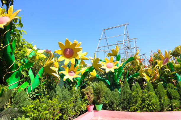 A vibrant garden features large artificial sunflowers, creating a cheerful and colorful display against a clear blue sky.