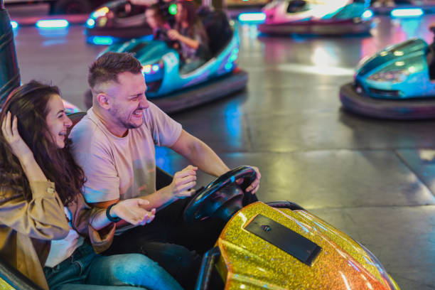 istock Joyful Couple Having Fun at Amusement Park Boyfriend Driving Trying to Avoid Hitting Bumper Cars 2199382589