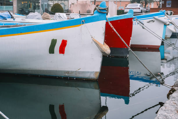 A cozy Italian waterfront with vibrant fishing boats reflecting on the calm water. Charming old houses with colorful facades create an atmosphere of warmth and European charm.