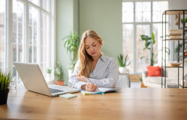 istock Young woman enjoying a cozy moment at home while writing in her notebook at a stylish table 2199386493