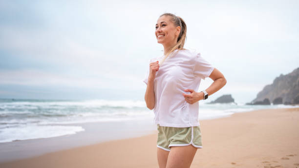 istock Woman jogging along sandy beach shoreline in morning 2199386617