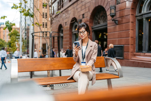 istock Young Asian Businesswoman Using Her Phone While Eating A Salad During Lunch Break On The Bench On The Street In Sydney In Australia 2199392284