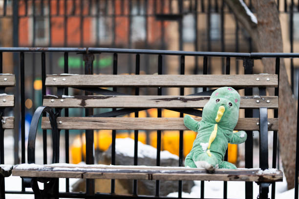 A green stuffed animal is sitting on a bench in the snow. The bench is empty and the scene is quiet