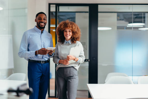 istock Two smiling young businesspeople holding digital tablet and documents standing in modern office 2199394975