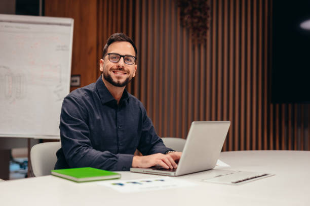 istock Businessman working on laptop in modern office, smiling at camera 2199395097
