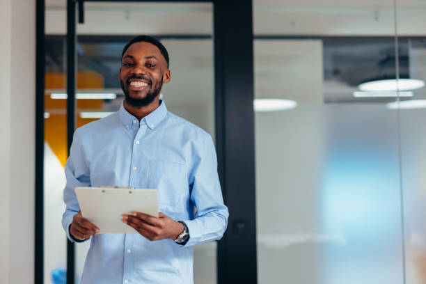 istock Smiling businessman holding clipboard standing in modern office 2199395195