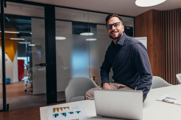 istock Businessman smiling sitting on meeting table working with laptop and graphs 2199395300