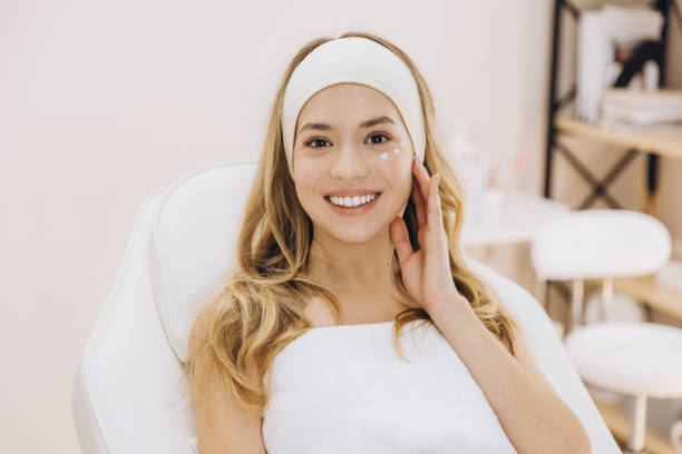 istock Beautician spreading moisturizing cream on client's face during professional skincare treatment at spa 2199396795