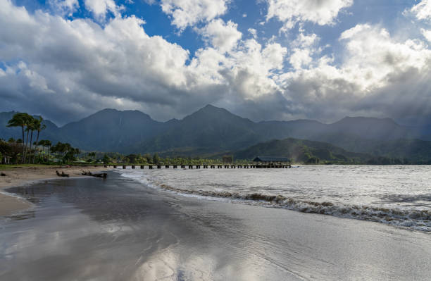 Hanalei Pier and beach are framed by dramatic mountains and sky in this scenic view of the north shore of Kauai.
