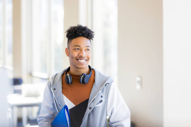 istock Happy young student smiling while carrying folders in school 2199398236