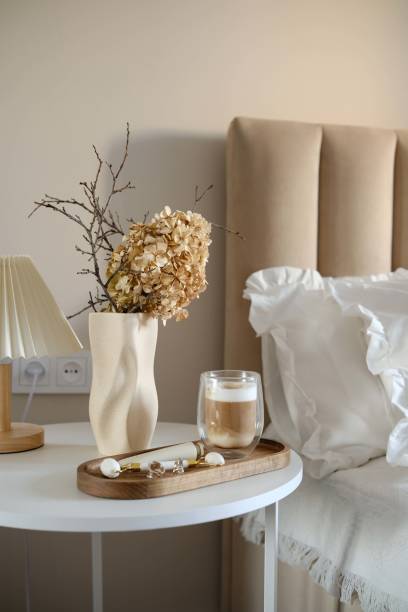 istock A calm and serene morning bedroom scene displays a chic bedside white round table complete with an elegant dry branches and flowers, a refreshing coffee drink, wooden tray with cosmetic accessories. 2199398642
