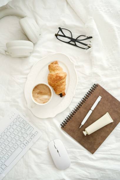 istock A serene workspace with coffee, a croissant, and essential tech items - keyboard, headphones, notebook to boost productivity and creativity on white fabric background. 2199398845