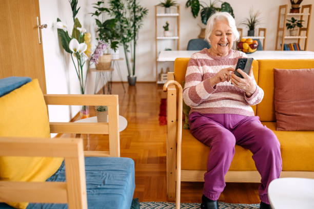 istock Old woman spending time at home sitting on sofa and looking at mobile phone 2199399001