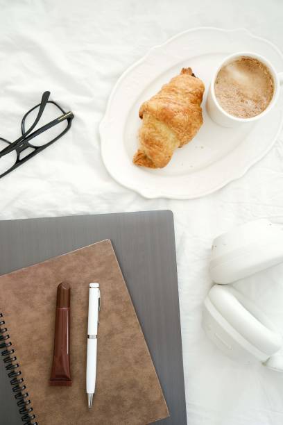 istock A serene scene with delicious coffee, a flaky croissant, laptop, notebook, pen, lipstick, headphones, glasses on white fabric. 2199399439