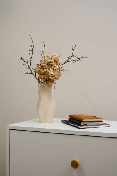 istock A chic and stylish vase with dry flowers with books on white table. 2199400404