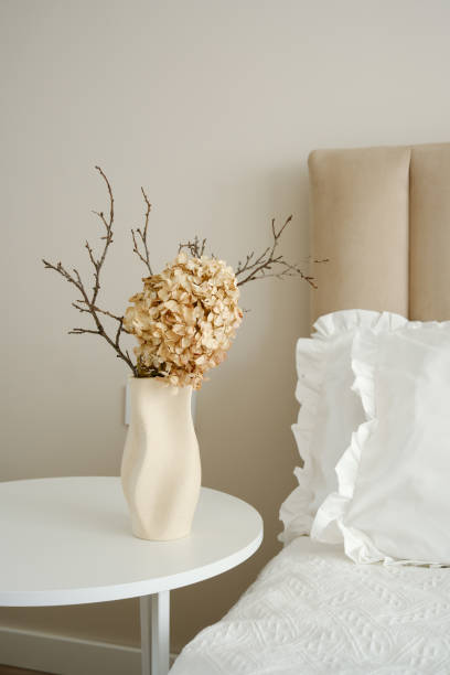 istock Elegant vase with dry branches and flower on white table near light bedside. 2199401002