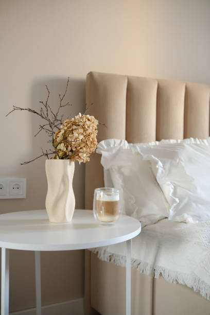 istock A calm and serene morning bedroom scene displays a chic bedside white round table complete with an elegant dry branches and flowers, a refreshing coffee drink. 2199401197