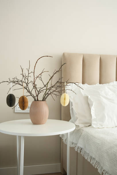 istock Elegant vase with dry branches, easter eggs on white table near light bedside. 2199403544
