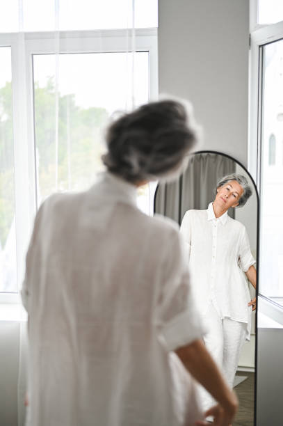 istock Happy mature woman looking at her reflection in a mirror at home 2199403697