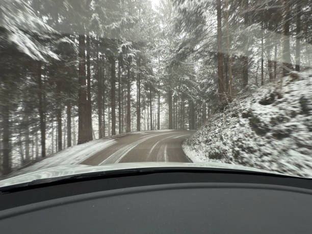 A captivating point-of-view shot from inside a car driving through a winding snow-covered forest road. The snow-dusted trees and curved road create a scenic and immersive experience, highlighting the beauty and challenges of winter driving. Perfect for themes related to road trips, adventure, seasonal landscapes, and travel safety.