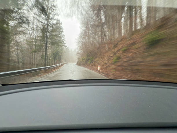 A dynamic motion blur perspective of driving on a winding road through a foggy forest, seen from inside a car. The blurred edges convey speed and movement, while the misty atmosphere enhances the feeling of adventure and mystery. This image represents road trips, nature exploration, and the challenges of driving in low-visibility conditions.