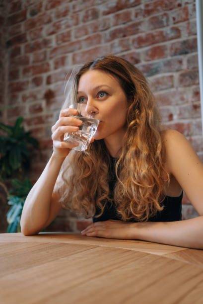 istock Woman Drinking Water from Glass at Table in Cozy Cafe 2199407553