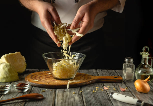 istock Hands skillfully stir crisp cabbage, aroma filling the air in the warmly lit kitchen. Ingredients and spices are artfully laid out on a wooden table, ready for a delicious meal. 2199415384