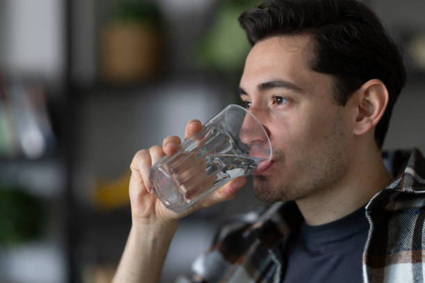 istock Young man drinking fresh water from a glass in his modern apartment 2199420791