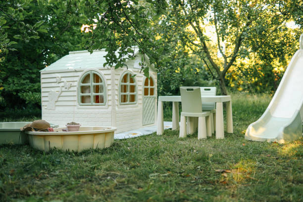 Children's backyard play area with a plastic slide, sandbox, table, chairs, and a small playhouse on the lawn. Perfect for outdoor fun, summer activities, and family entertainment.