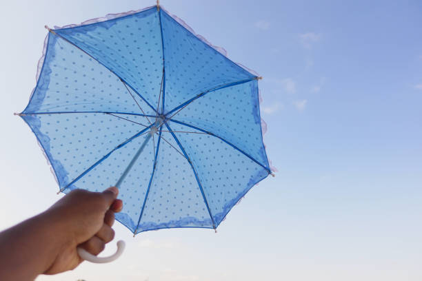 A vibrant blue umbrella adorned with playful polka dots, held up against a bright blue sky