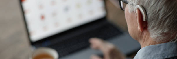 istock Header Image of Senior Man Wearing Hearing Aid Using Laptop Indoors 2199429961