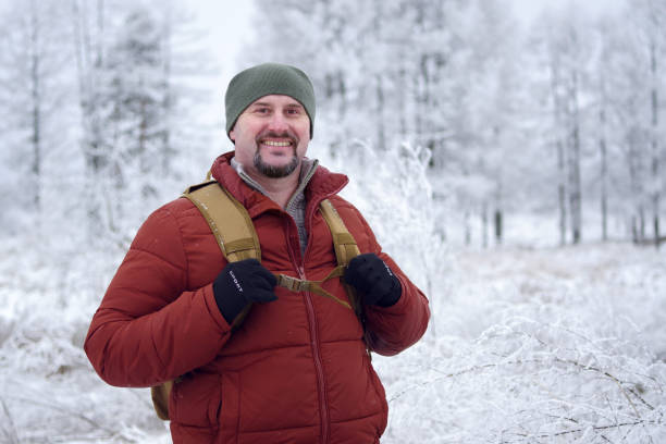 istock Smiling hiker wearing backpack enjoying snowy winter forest landscape. A positive bearded man smiles while looking at the camera during a winter walk outside the city 2199432056