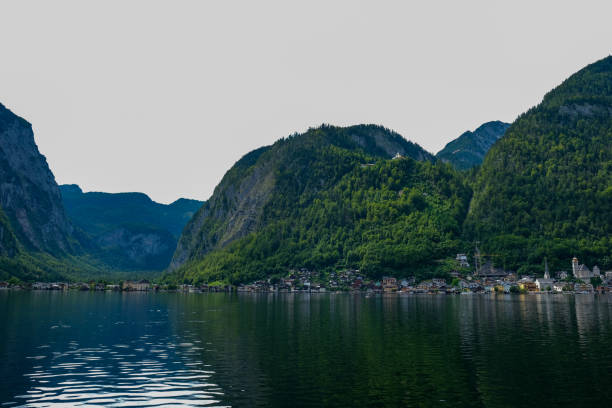 A breathtaking view of a charming lakeside village nestled between towering green mountains. The tranquil waters reflect the stunning landscape, creating a serene and picturesque scene.