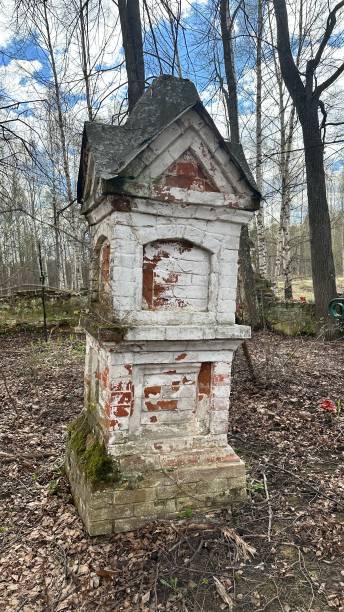 istock Small white building with a red roof sits in a forest. An abandoned ancient Russian cemetery in the woods with a wooden church. 2199435309