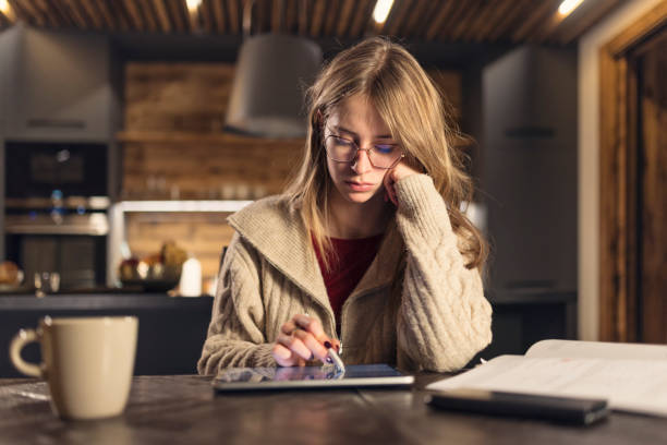 istock Young woman studying with a tablet and book in a modern kitchen 2199443966