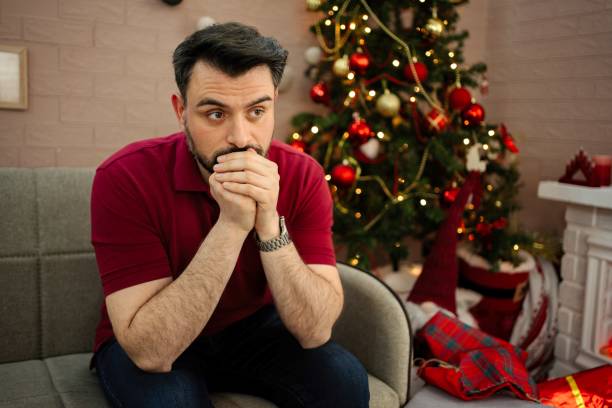 istock Sad man sitting on sofa near decorated Christmas tree at home 2199447644
