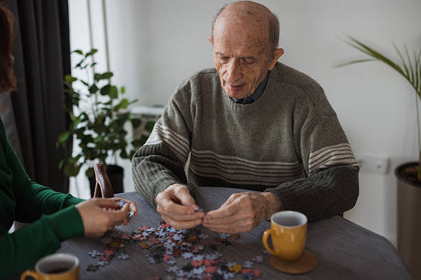 istock Elderly man getting a visit from volunteer in nursing home, playing puzzle 2199449972