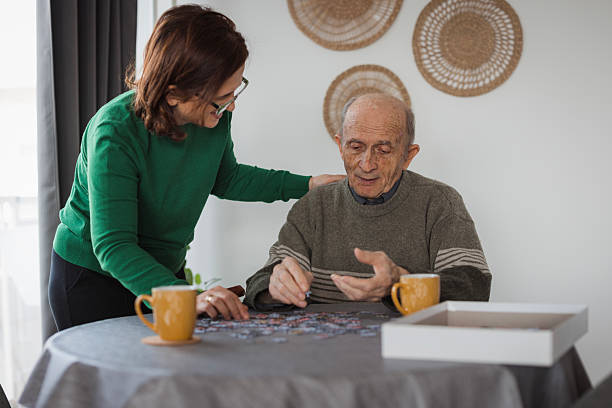 istock Elderly man getting a visit from volunteer in nursing home, playing puzzle 2199449975