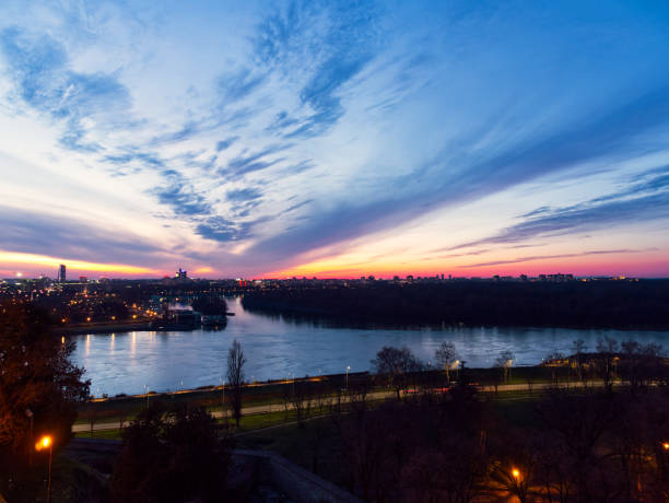 Aerial view of a city skyline at sunset with a river reflecting vibrant colors and dramatic sky