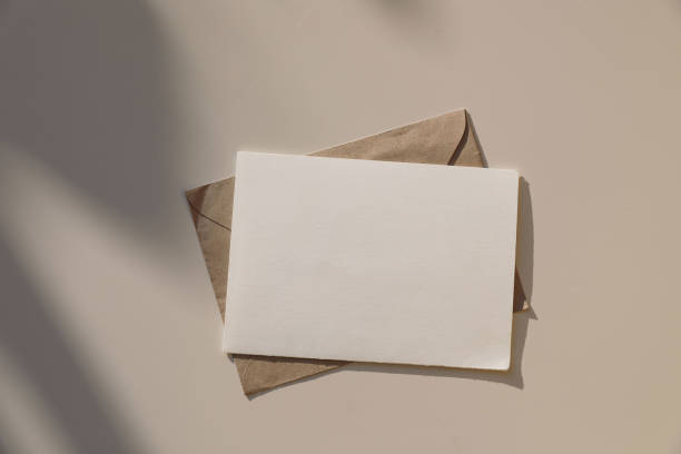 istock Blank horizontal greeting card, invitation mockup, craft envelope in sunlight on beige table background. Soft long floral shadows. overlay Neutral web banner. Elegant stationery template. Flat lay. Top view. 2199458839