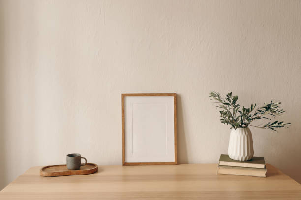 istock Summer interior still life. Blank wooden picture frame mockup. Modern interior, minimal scandinavian home design. Olive tree branches in vase, cup of coffee tea, books on table. Beige wall background. 2199458854