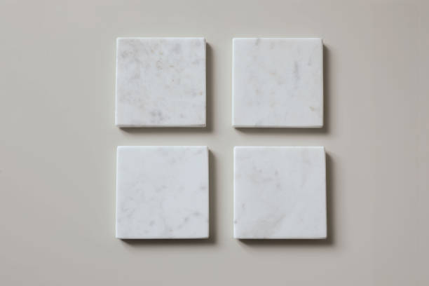 istock Four white square marble tiles coasters mockups isolated on textured beige wooden table background. Natural stone blocks, podiums objects. Creativity concept. Artwork template display. 2199459751