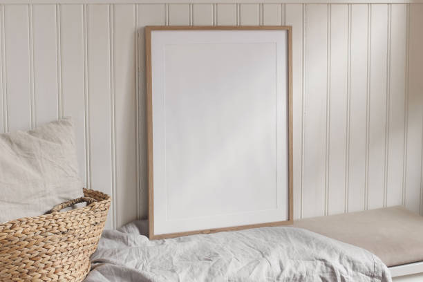 istock Empty vertical portrait A2 thin wooden frame mockups with linen cloth on bench. White beadboard wainscot wall paneling background. Straw French basket, linen pillow cushion. Scandinavian interior home 2199459753