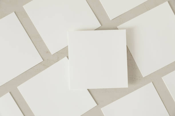 istock Many empty white square business card greeting card mockups with soft shadows lying diagonally on beige textured wooden table background. One card above. Flat lay, top view. Stationery composition. 2199459756