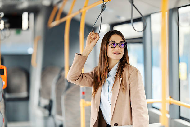 Portrait of fashionable young woman standing in public transportation, riding it and holding handle while looking trough the window.