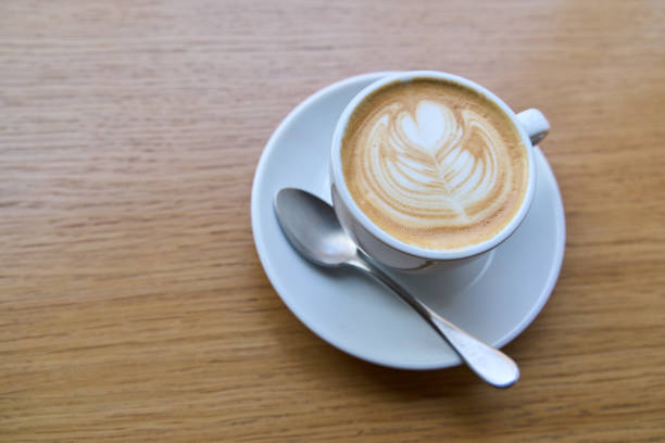 Latte art coffee sitting on wooden table with spoon